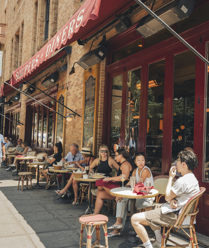 People dining outdoors at a restaurant with a red awning and "DINER'S" sign above.