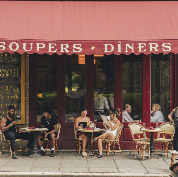 People dine al fresco at Soupers Diners, a cozy restaurant with red awning and tables under street lamps.