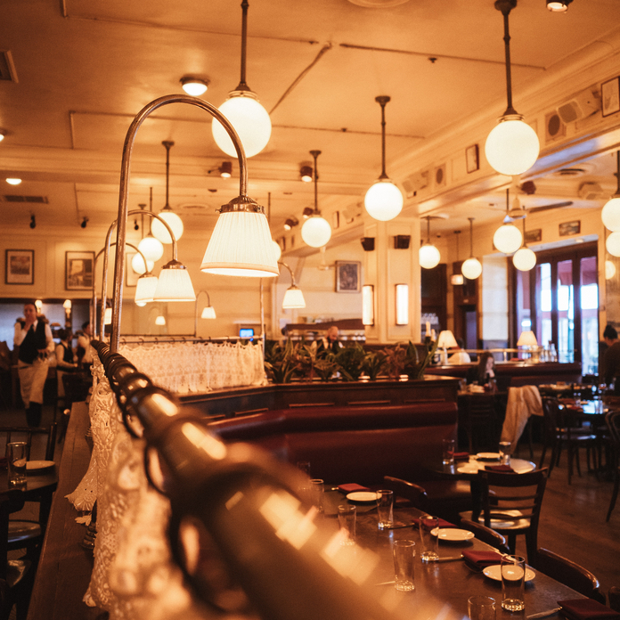 Cozy restaurant interior with warm lighting, hanging lamps, wooden bar, and white lace tablecloth.