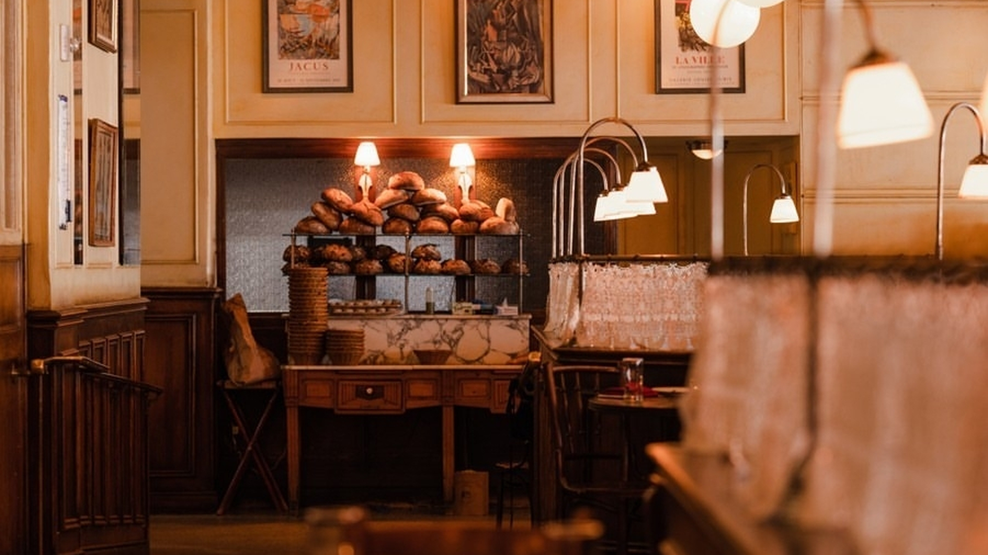 Cozy restaurant interior with warm lighting, wooden shelves, framed art, and a display of bread and pastries.