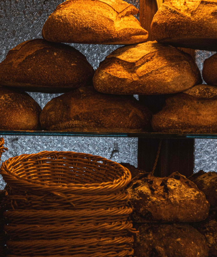 Freshly baked artisan bread loaves displayed on metal shelving with woven baskets in a bakery setting