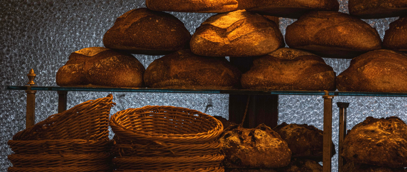 Freshly baked artisan bread loaves displayed on wire shelves with woven baskets in warm lighting